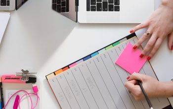 person holding pencil and stick note beside table
