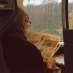 A woman reads a newspaper on a train.
