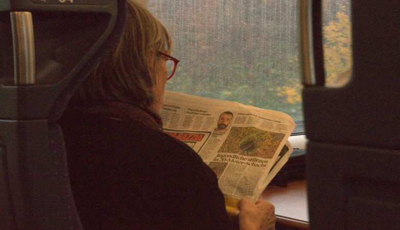 A woman reads a newspaper on a train.